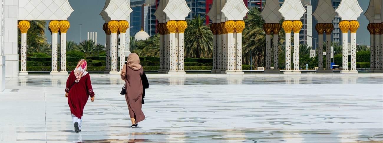 two people walking in front of a large white building with Sheikh Zayed Mosque in the background